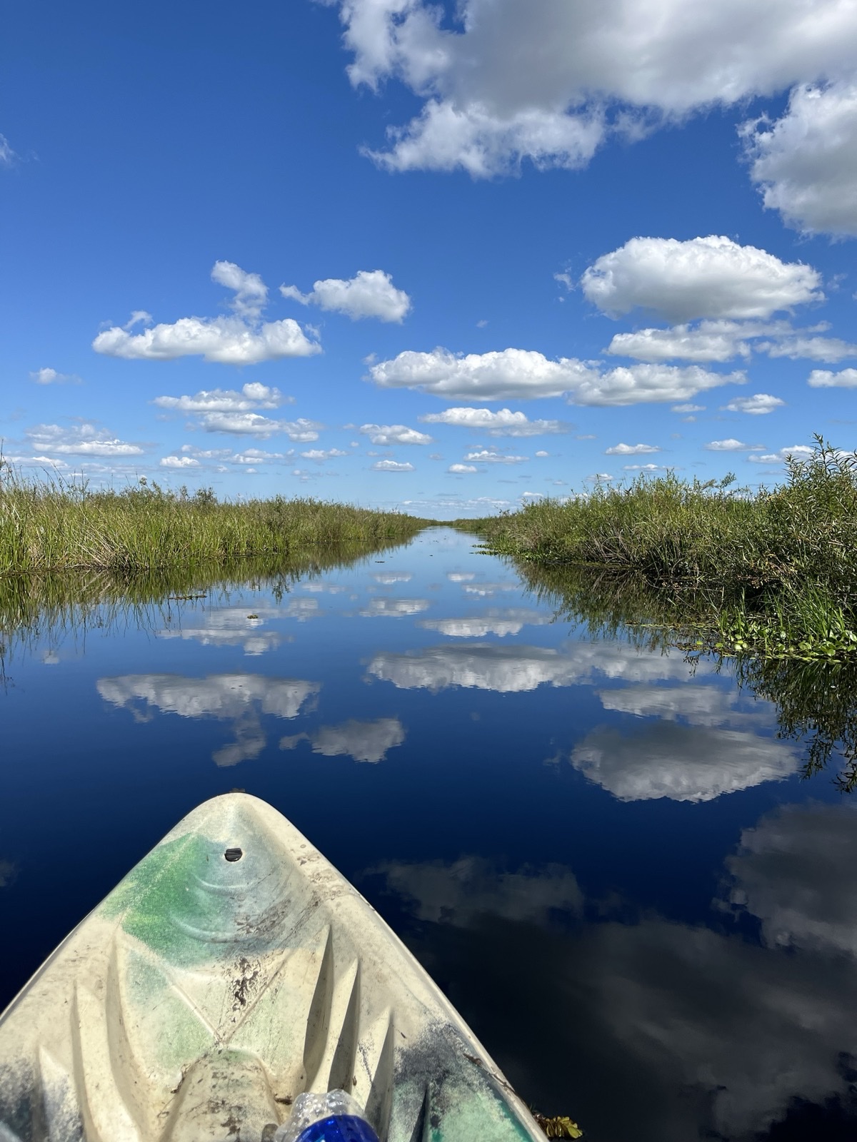 Proa de un kayak en un canal entre pajonales que refleja las nubes, Esteros del Iberá