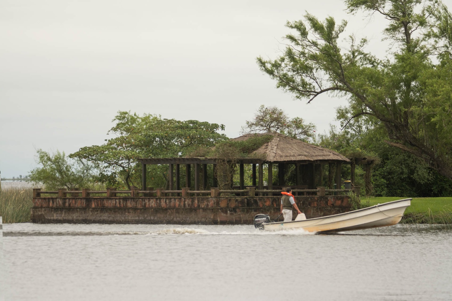 Lancha pasando frente al quincho de techo de paja en la Laguna Iberá, Carlos Pellegrini
