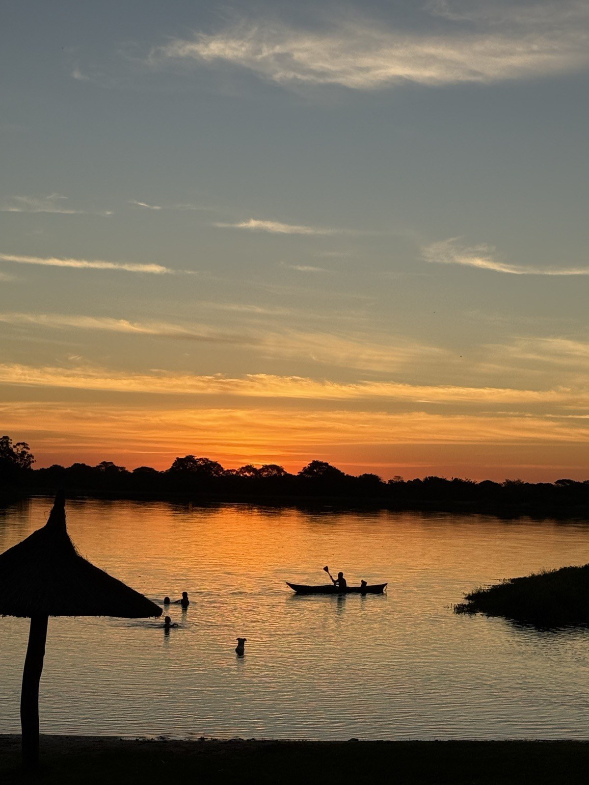 Atardecer en el balneario de Loreto con bañistas y canoa en el agua, Corrientes