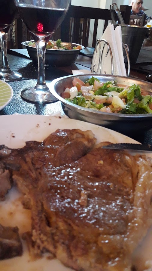 Bife jugoso con ensalada mixta y copa de vino tinto en la mesa de Karuhá