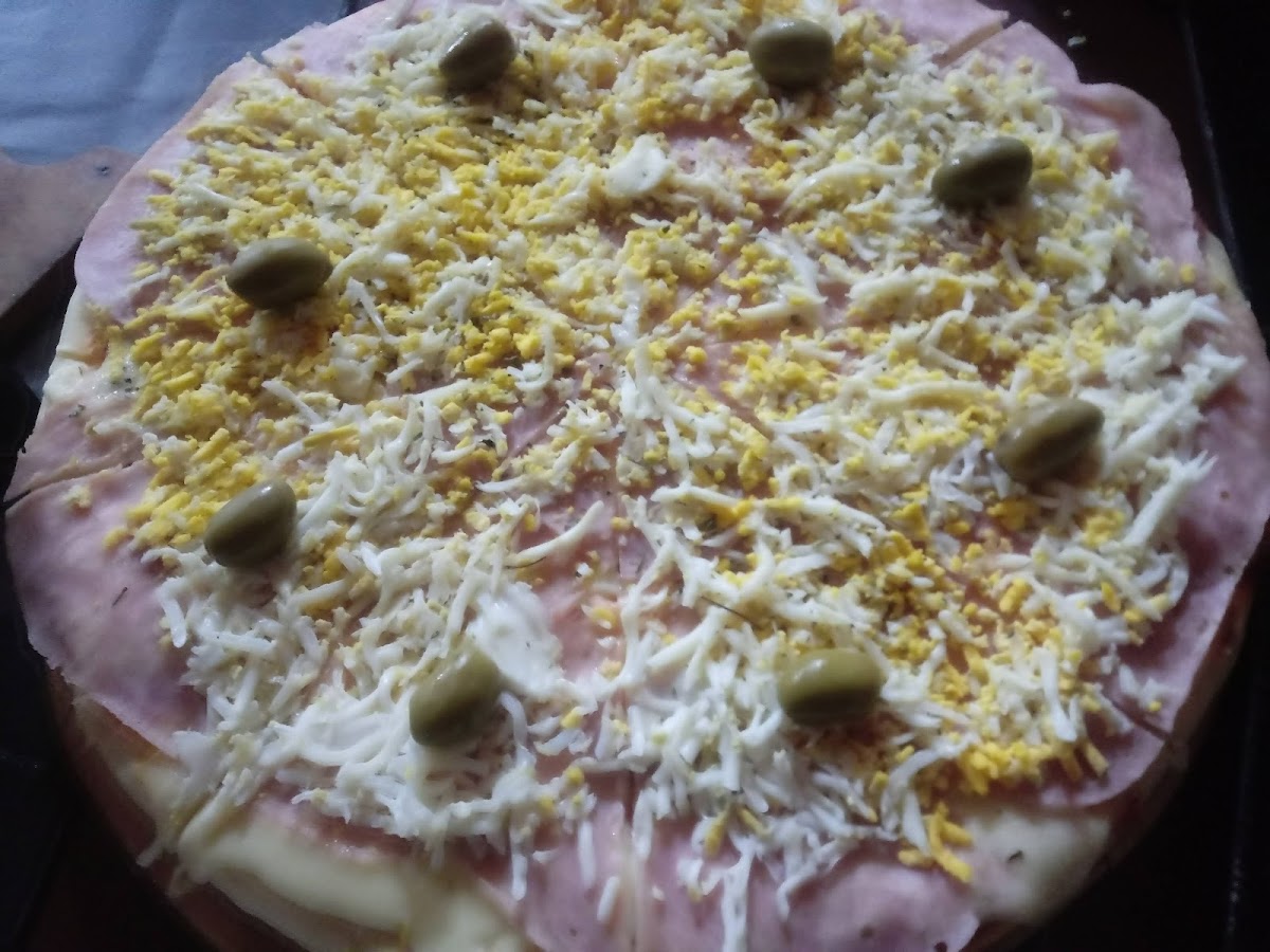 Pizza casera con jamón, mozzarella y aceitunas, lista para hornear
