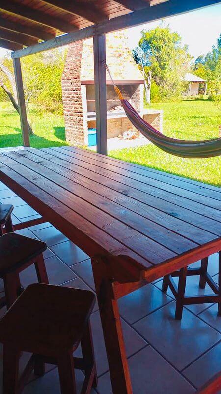 Galería con mesa de madera, hamaca y asador al fondo