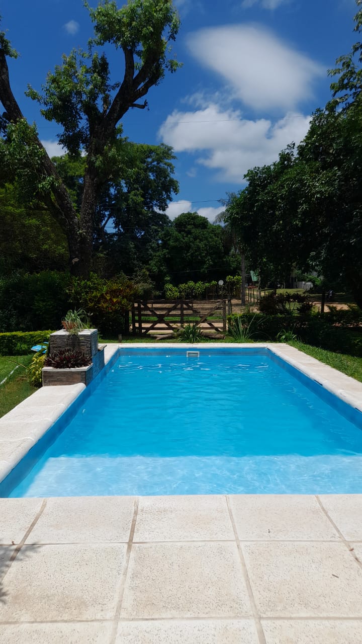La pileta al sol, con la tranquera y el monte atrás