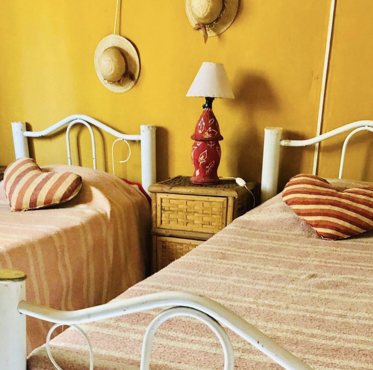 Habitación twin con pared ocre y sombreros