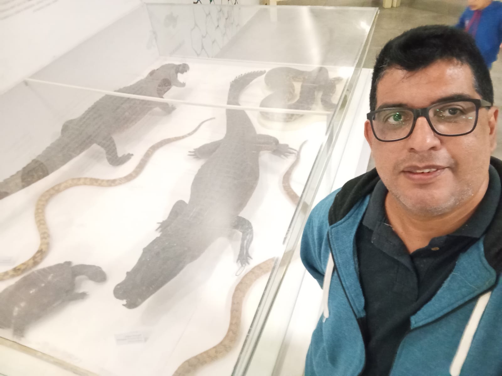In front of a display case of caimans and snakes at a wildlife exhibit