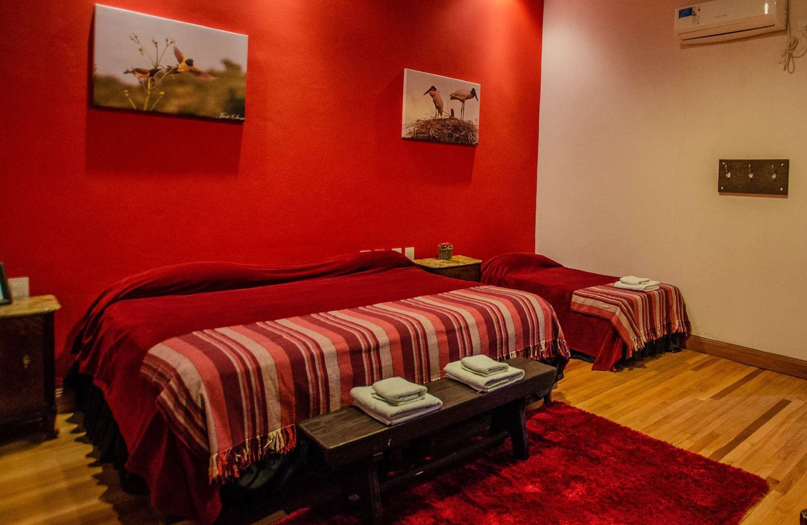Habitación de pared roja con dos camas y cuadros de aves