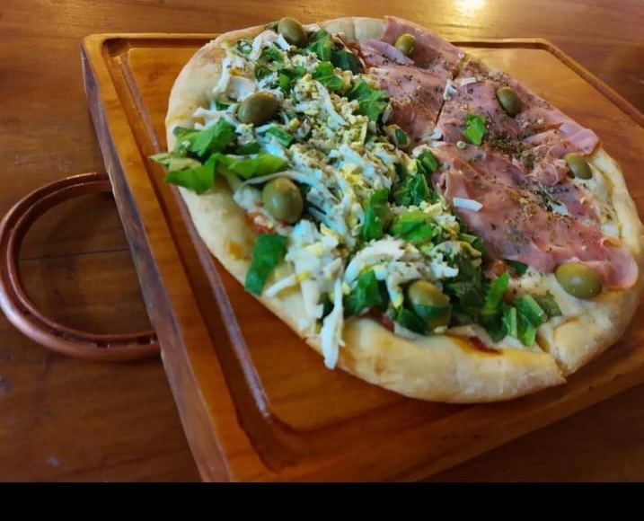 Pizza con jamón, rúcula, huevo y aceitunas sobre tabla