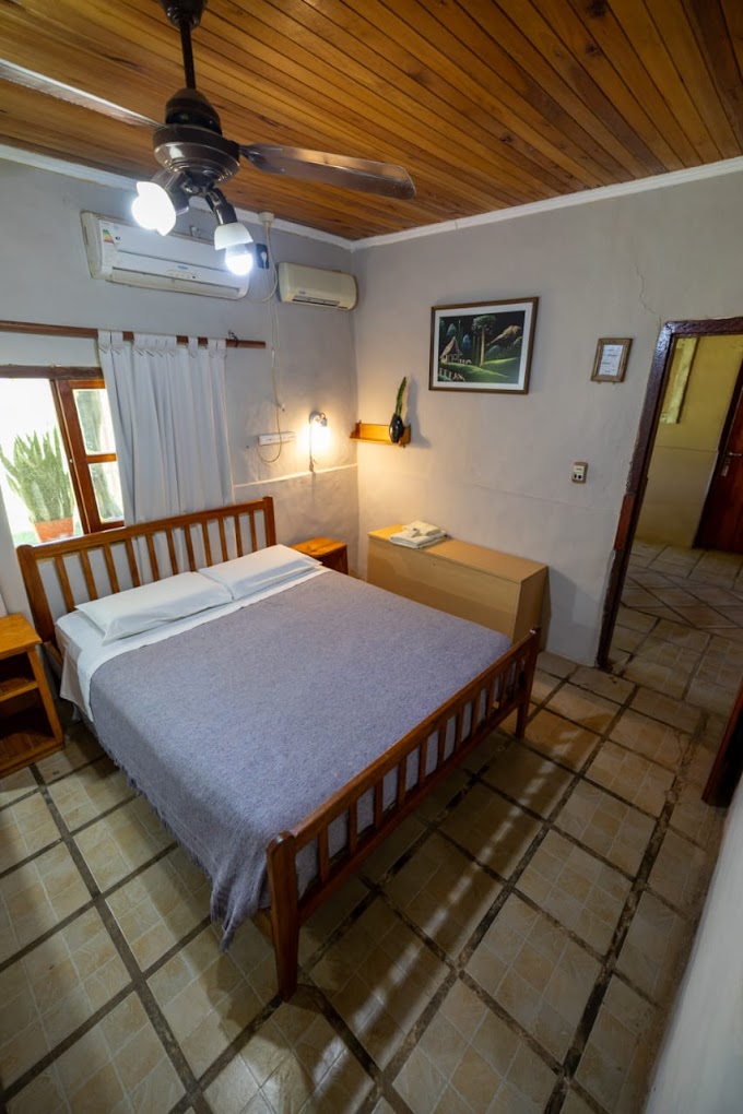 Habitación con cama de madera, techo de cedro y ventilador en la Posada Rancho Jabirú