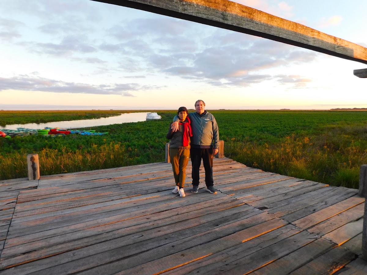 Pareja en muelle de madera al atardecer con kayaks de colores al fondo